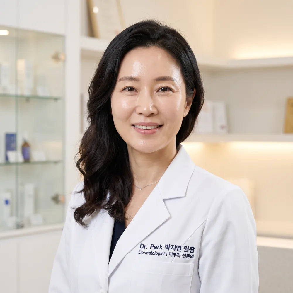 A smiling woman with dark hair wearing a white lab coat stands in a brightly lit office.